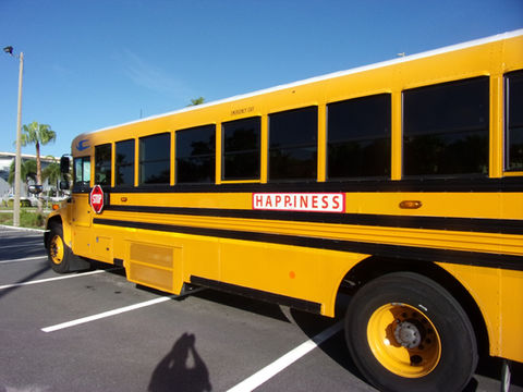 A yellow Florida school bus with a red HAPPINESS sign mounted on its side, palm trees visible in the background